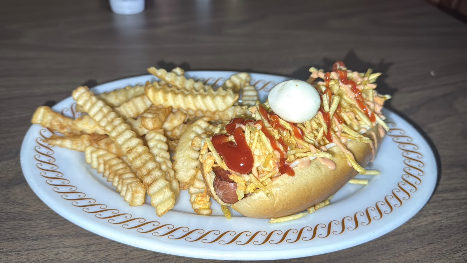 Perra caliente cubierta con salsas y acompañada de papas fritas